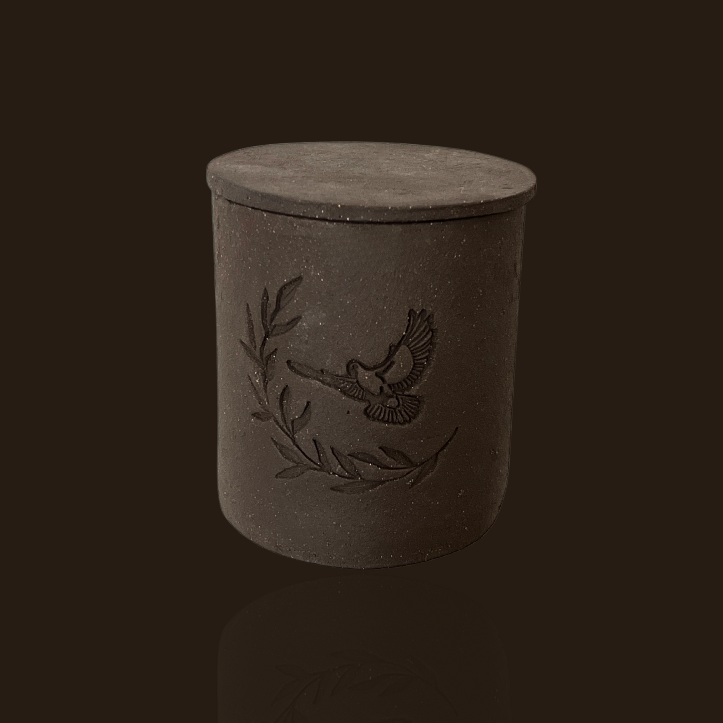 Dark gray cylindrical container with bird and laurel wreath design on a black background