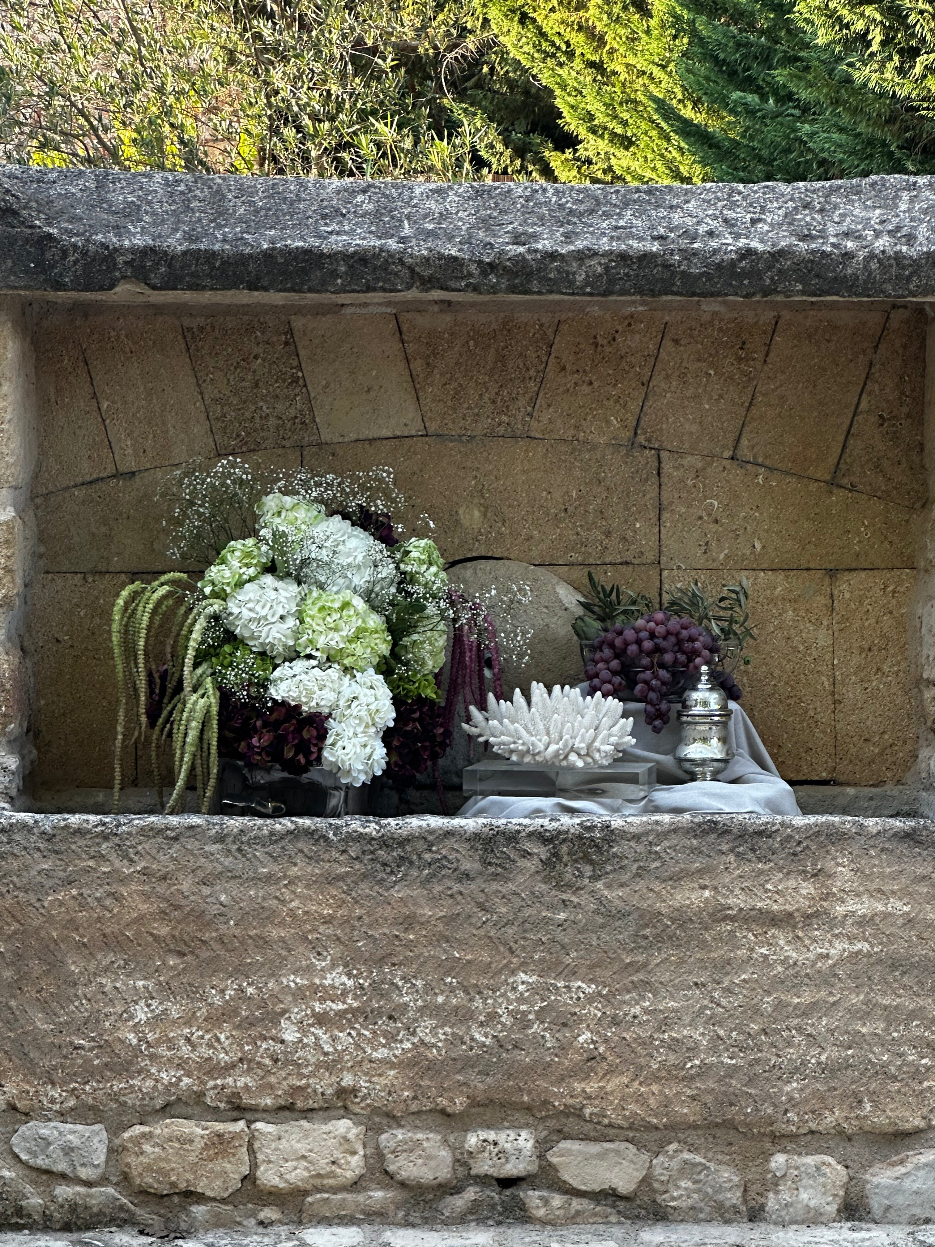 Decorative stone shelf with flowers and a teapot against a stone wall.