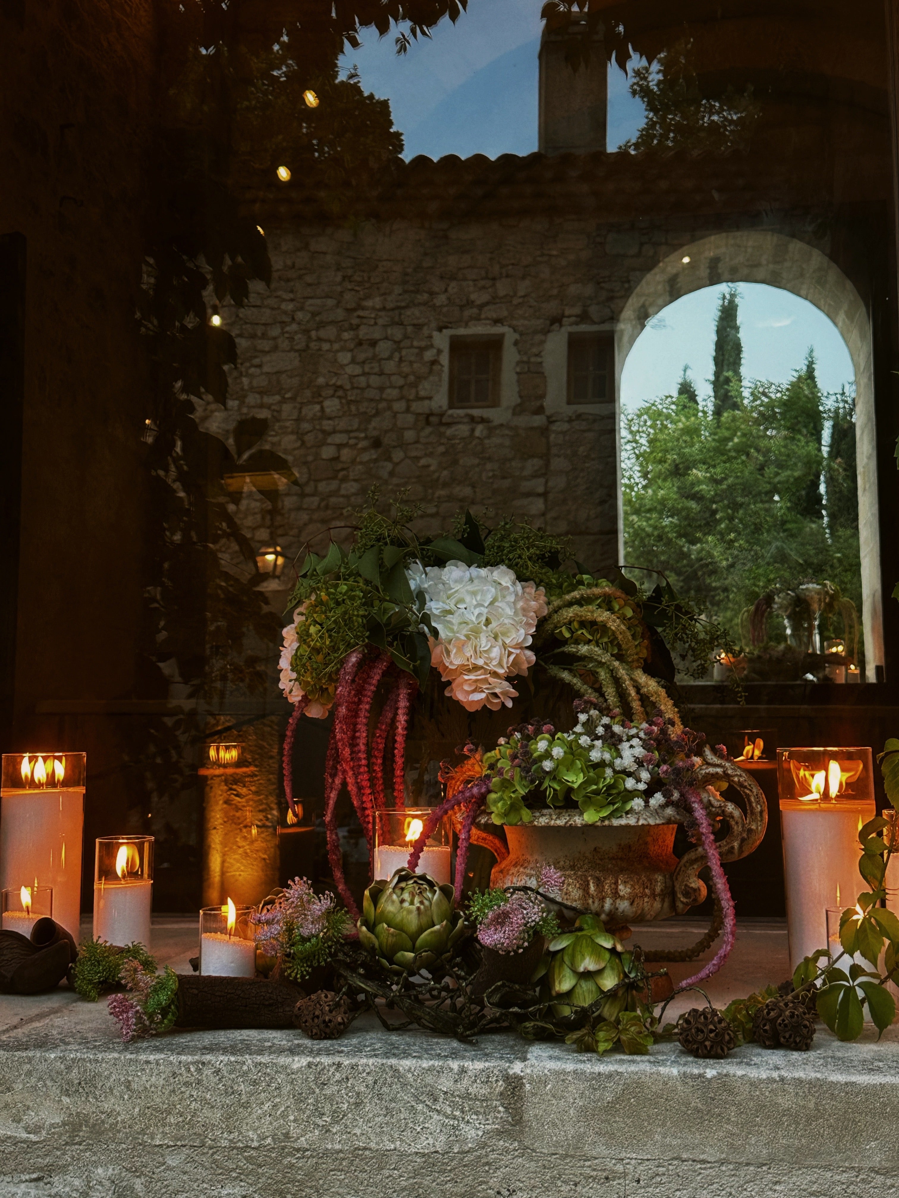Decorative outdoor setting with candles and flowers in a stone-walled garden.