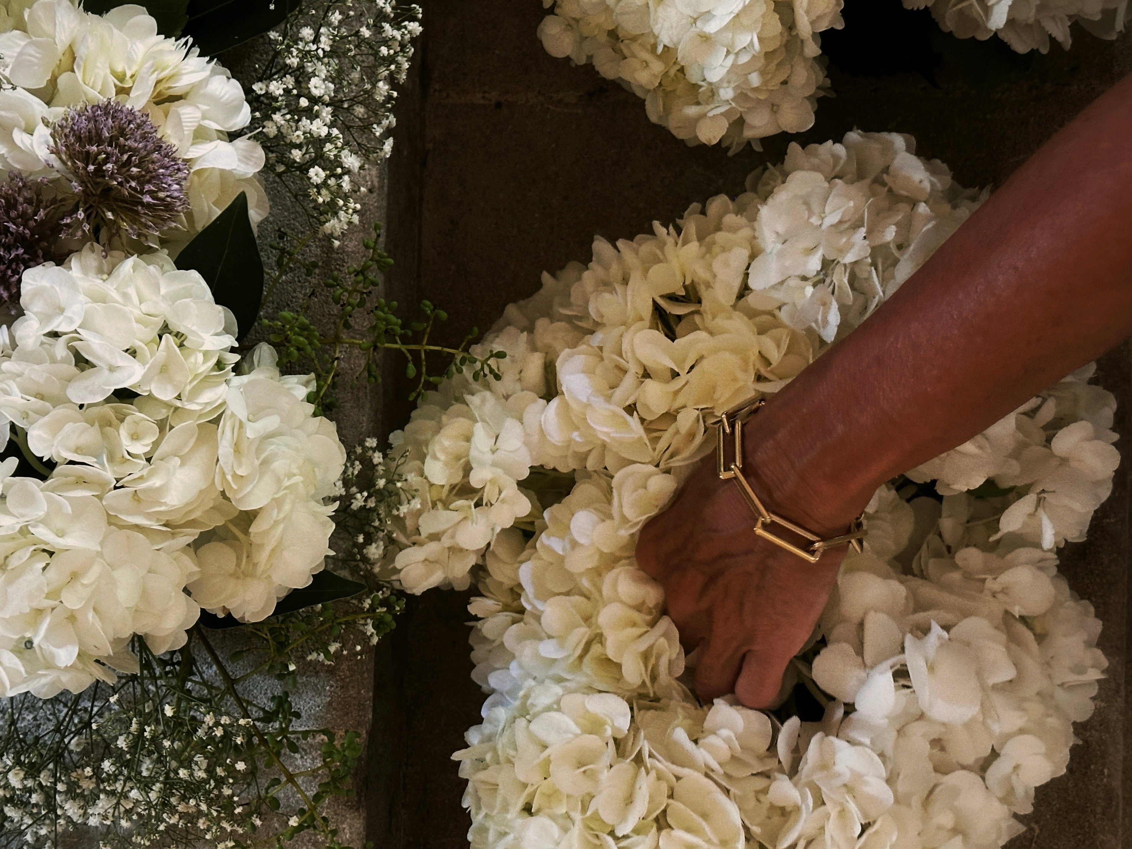 Close-up of a hand wearing a gold bracelet on a floral wreath.